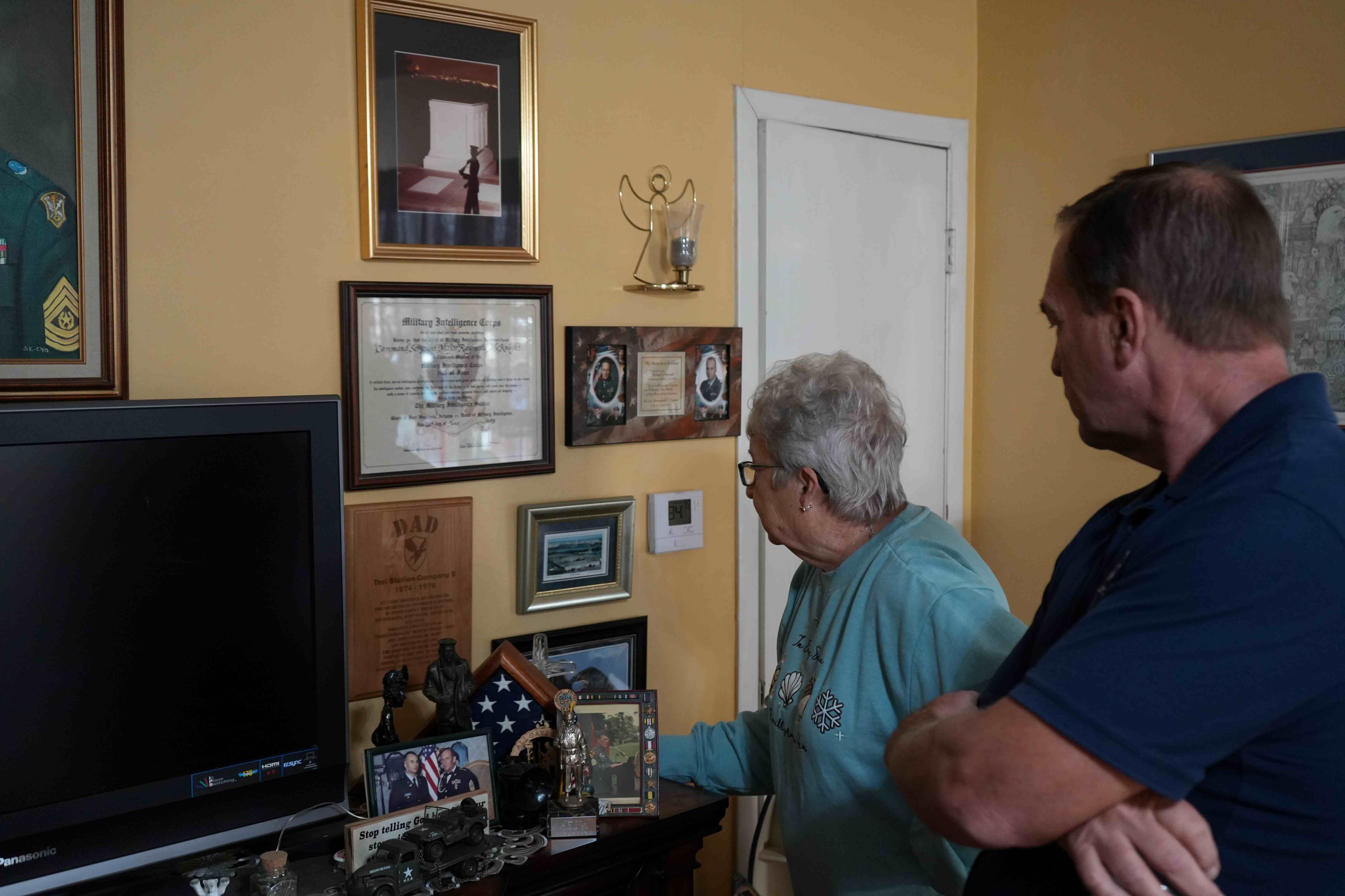 A woman showing a man photos on a wall inside a house.