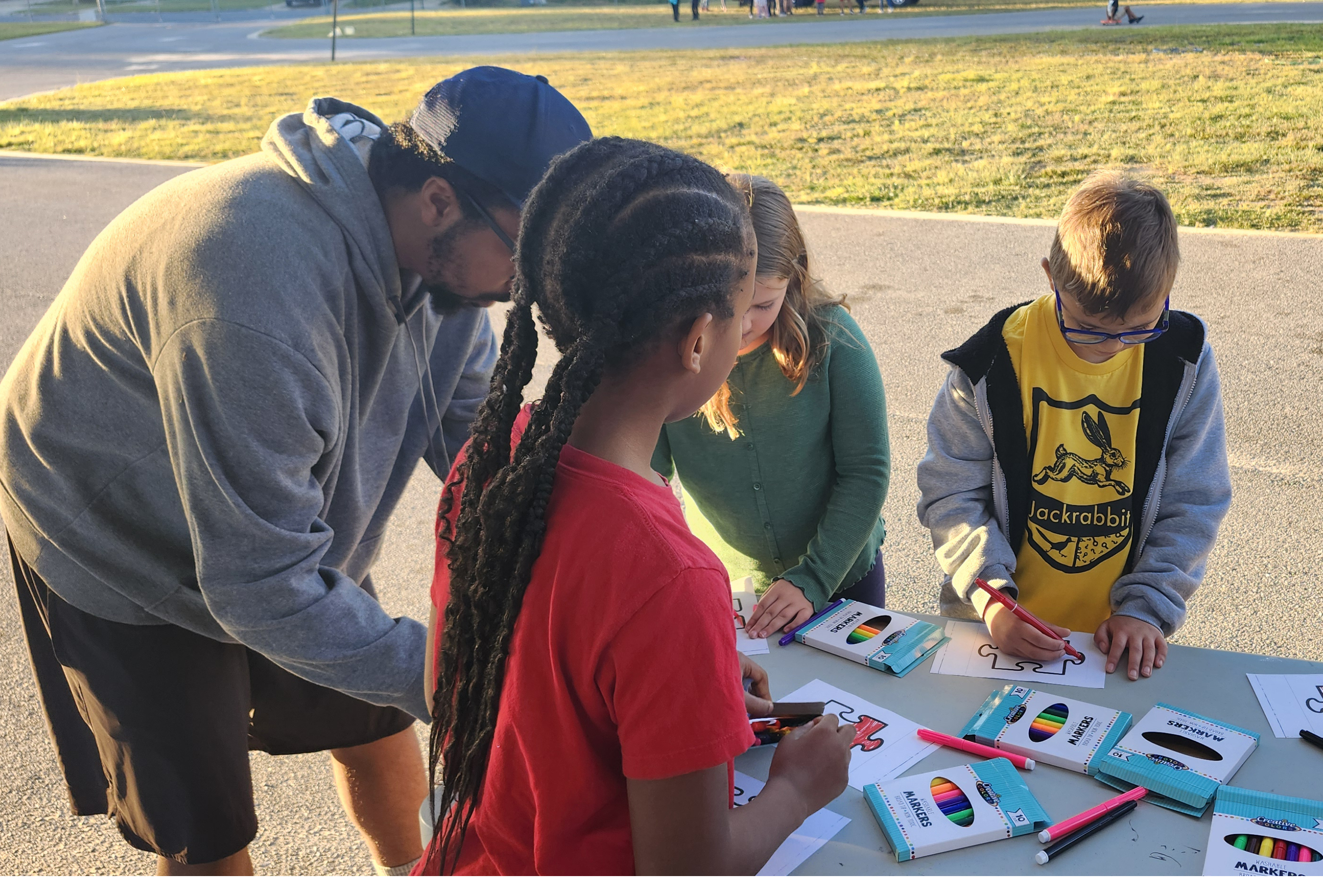 Kids coloring outside at a table with an adult.