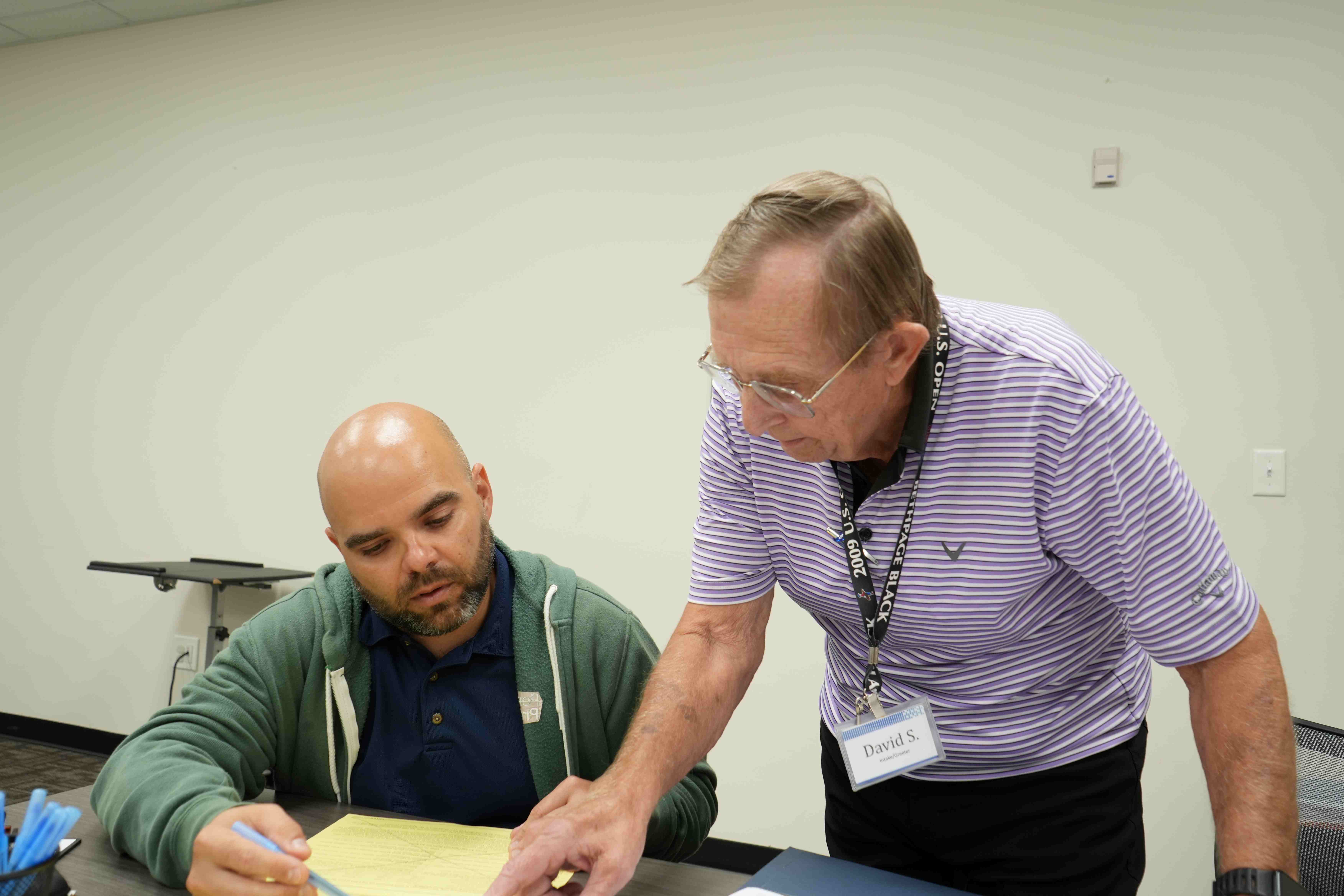 An older man helping a younger man with paperwork.