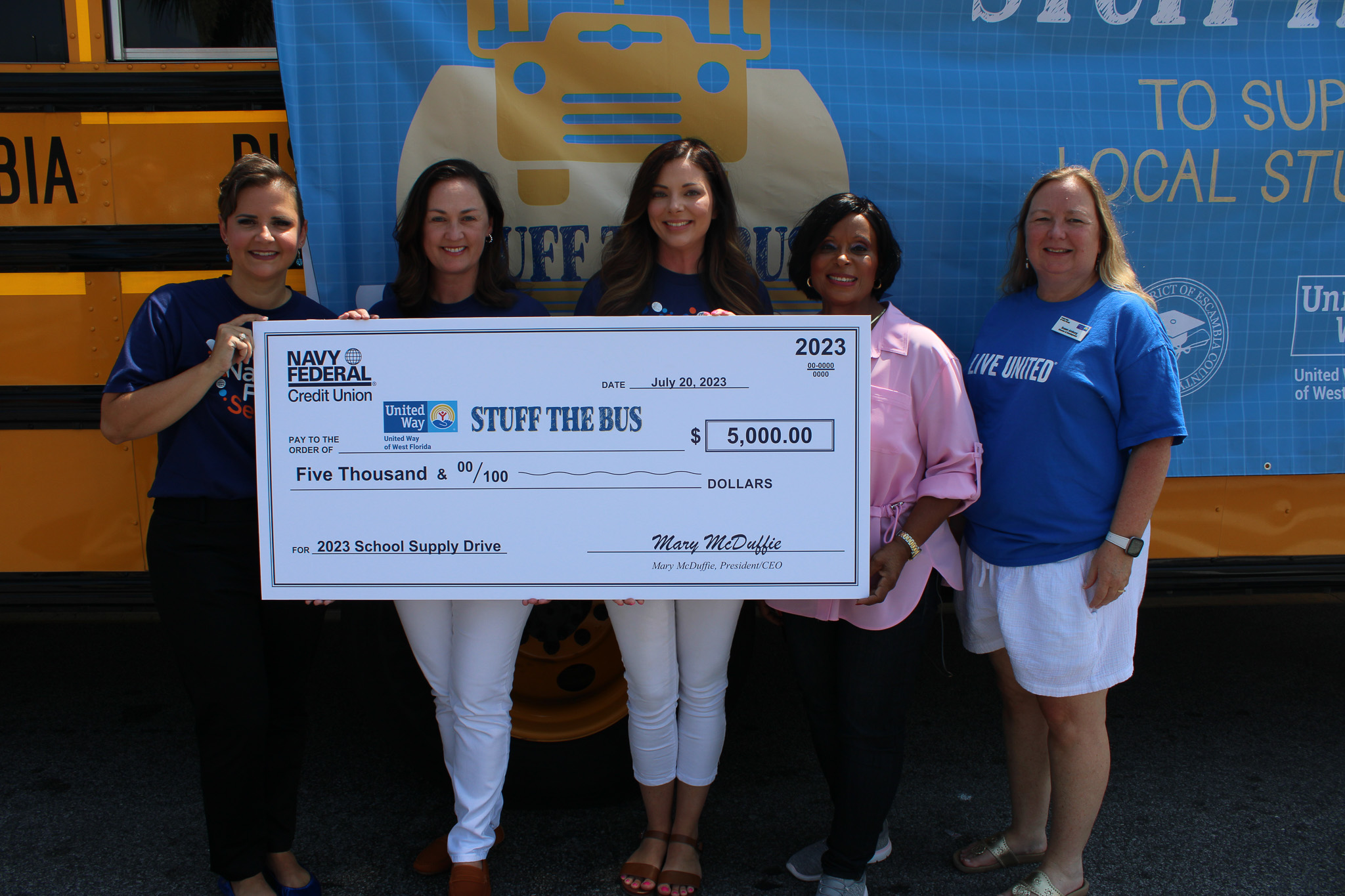 Navy Federal Employees holding $5,000 check in front of Stuff the Bus Bus