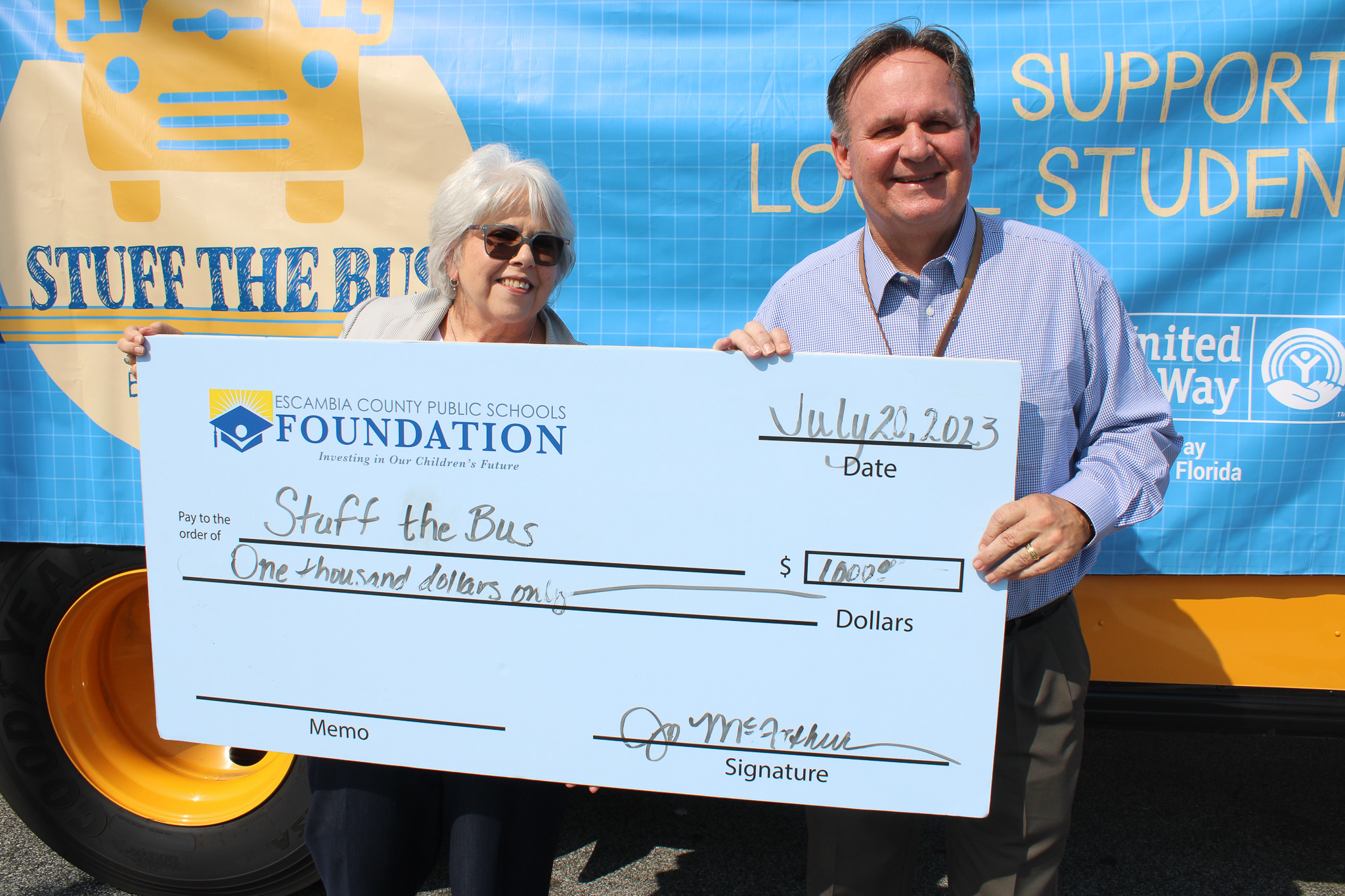 Escambia County Public School Foundation holding $1.000 check in front of Stuff the Bus Bus