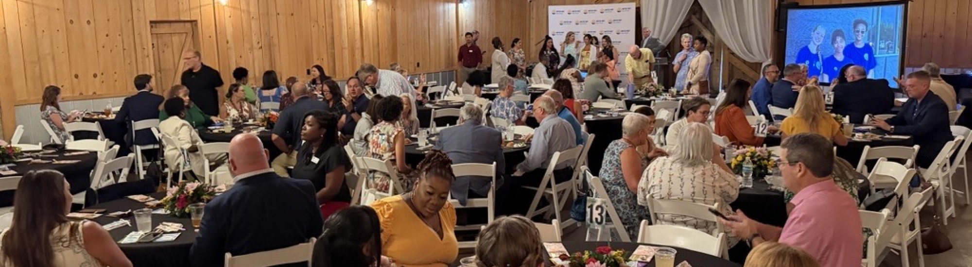 Many people sitting around many tables inside a barn.
