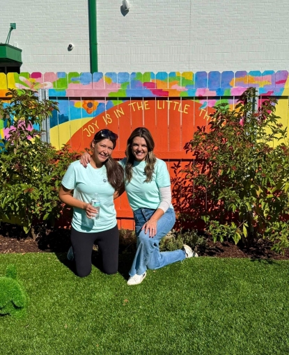 Girls smiling in front of a painted fence.