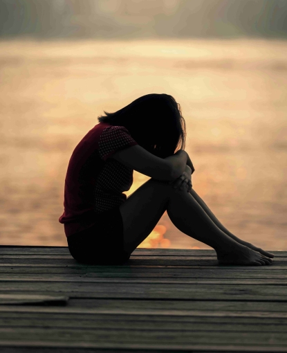 woman sitting by herself on a dock with her head on her knees, looking sad.