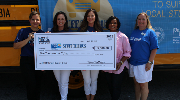 Navy Federal Employees holding $5,000 check in front of Stuff the Bus Bus